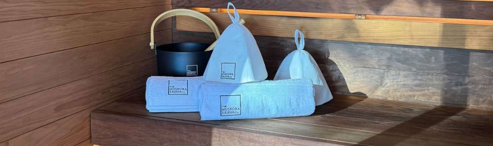 Muskoka Sauna interior with traditional Finnish sauna accessories including wooden bucket, ladle, and felt hat on cedar bench with modern LED accent lighting.