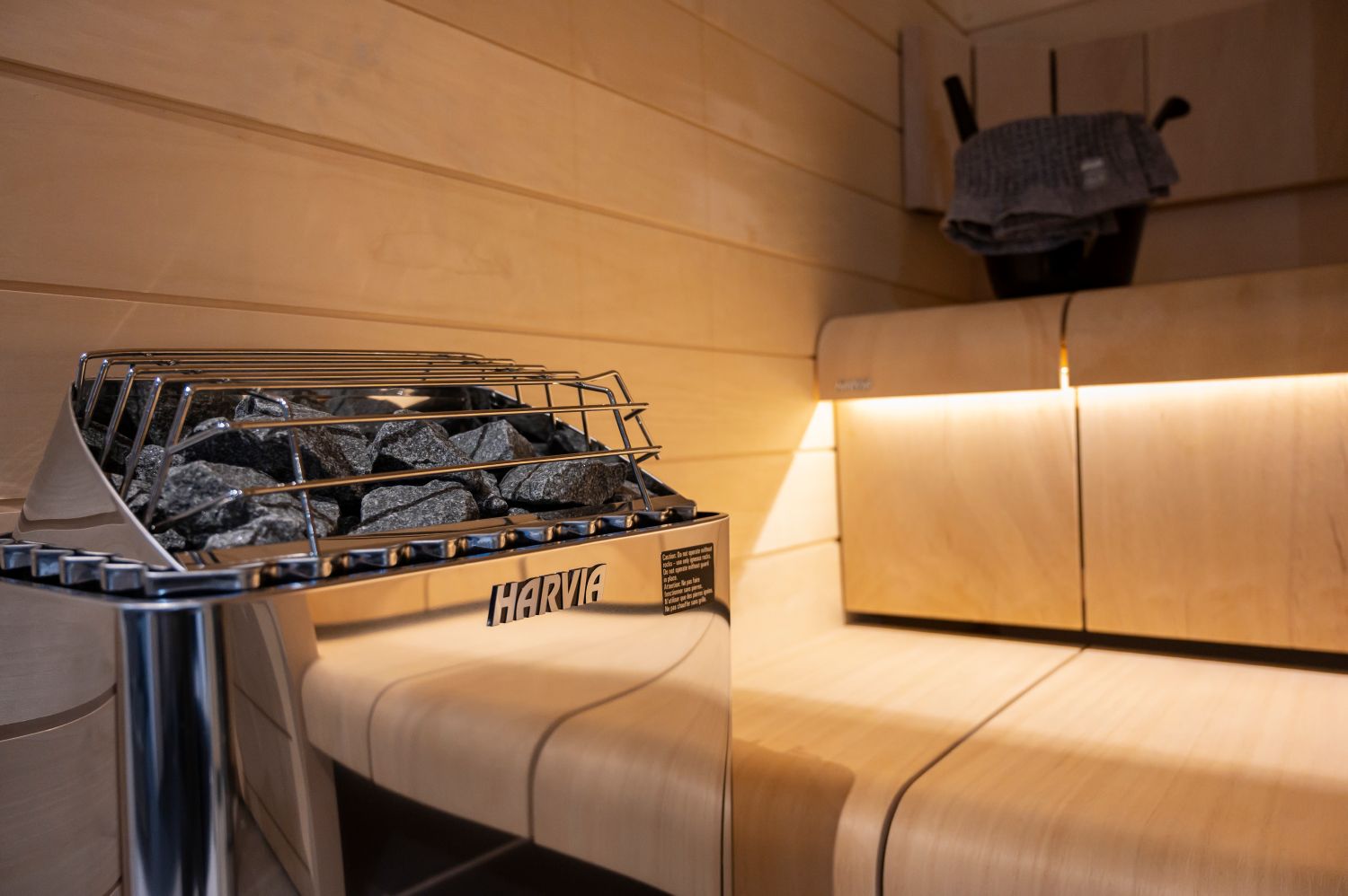 Harvic grill in a wooden sauna with a bench and towel hanging on the wall.
