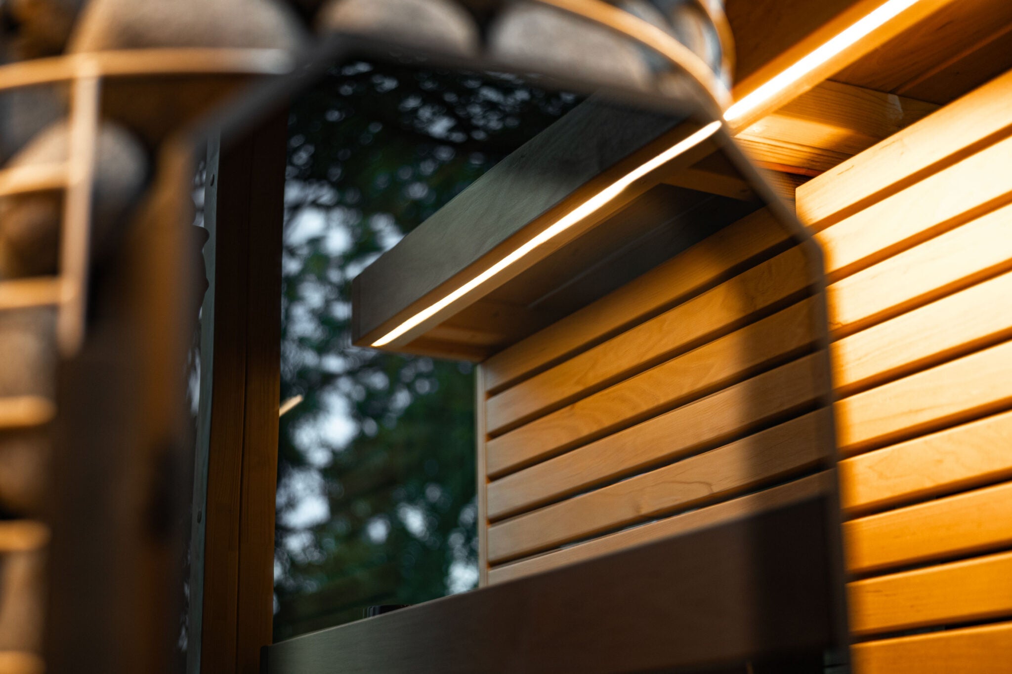 Modern outdoor light fixture on a wooden wall with blurred greenery in the background
